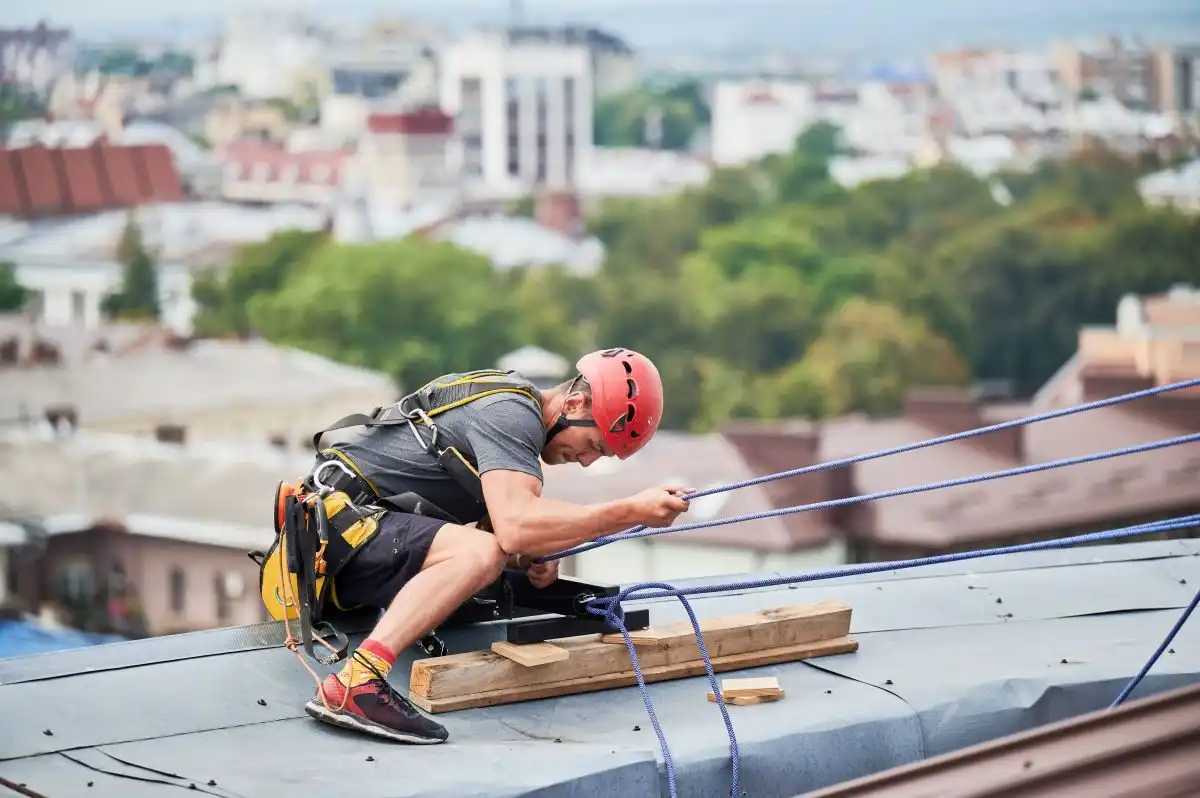 Alpinist utilitar care lucrează pe un acoperiș plat, cu orașul în fundal