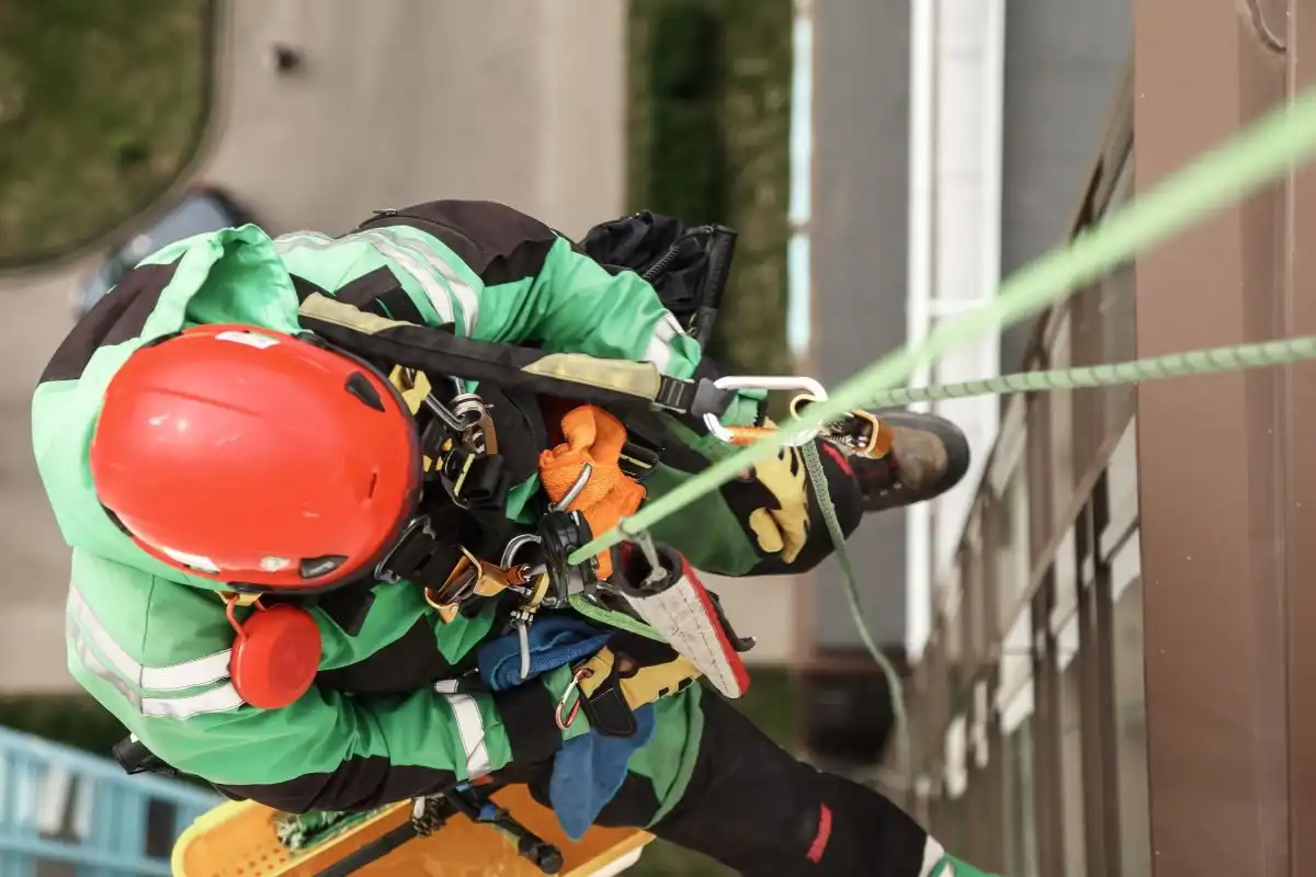 Alpinist utilitar cu cască roșie văzut de sus, coborând pe fațadă
