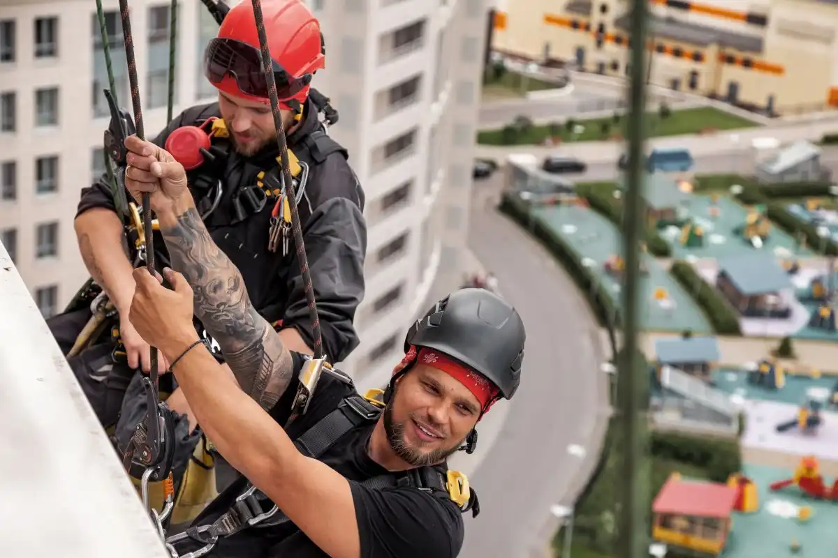 Doi alpiniști utilitari care pregătesc coborârea pe fațada unui bloc