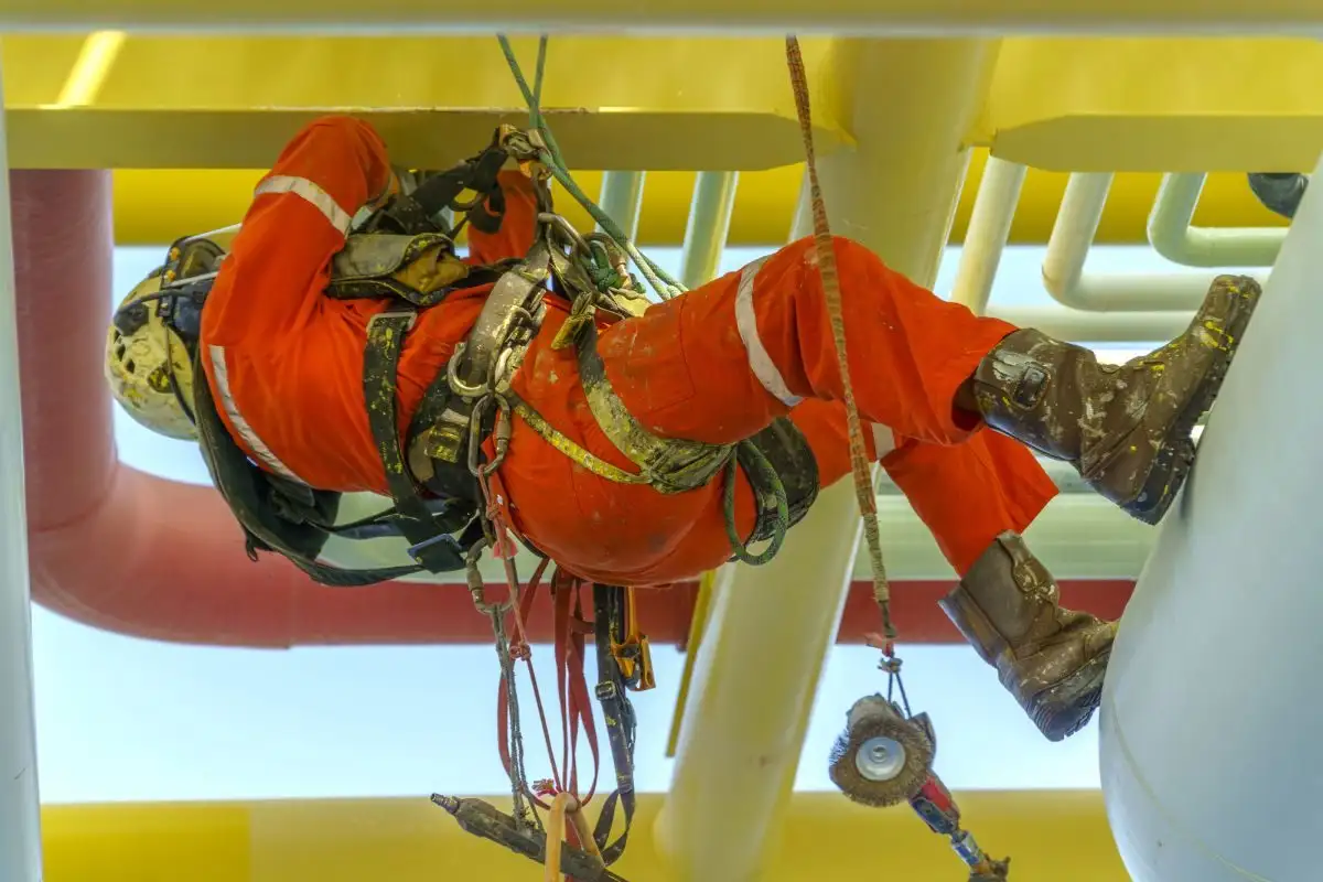 Alpinist utilitar în salopetă portocalie printre conducte industriale