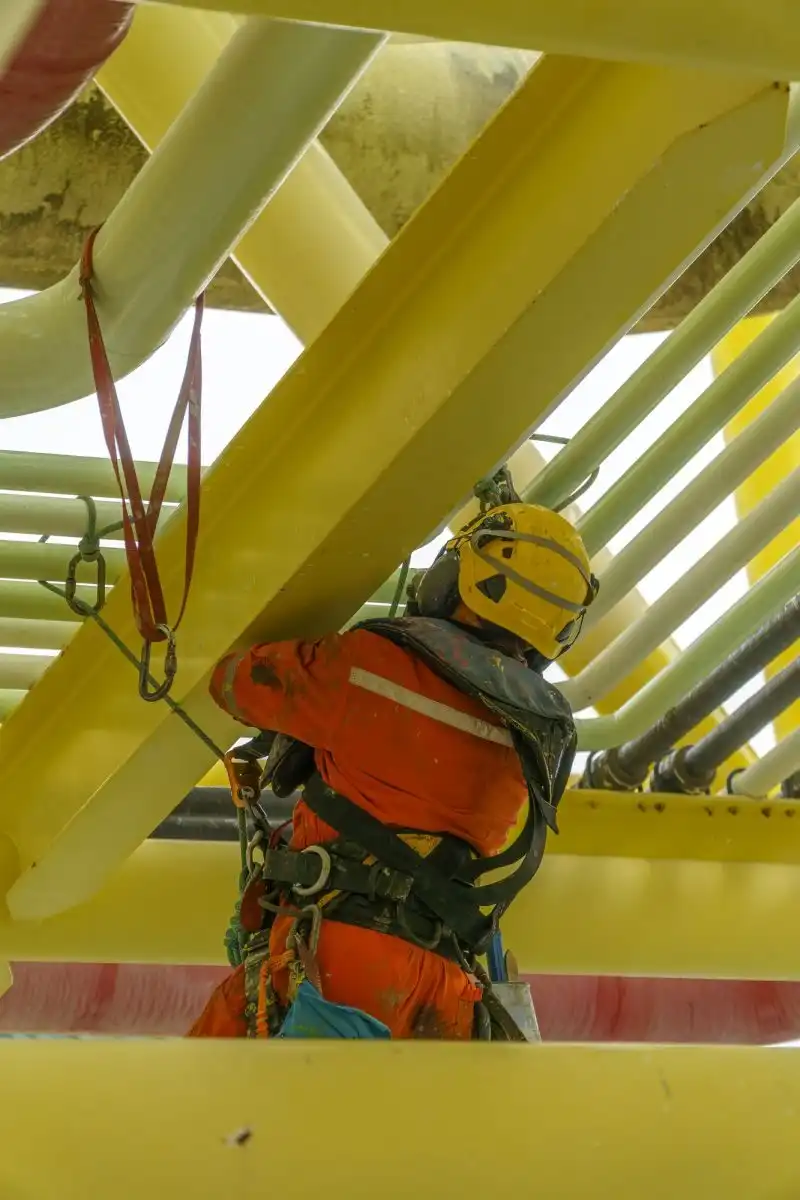 Alpinist utilitar suspendat într-o structură industrială galbenă
