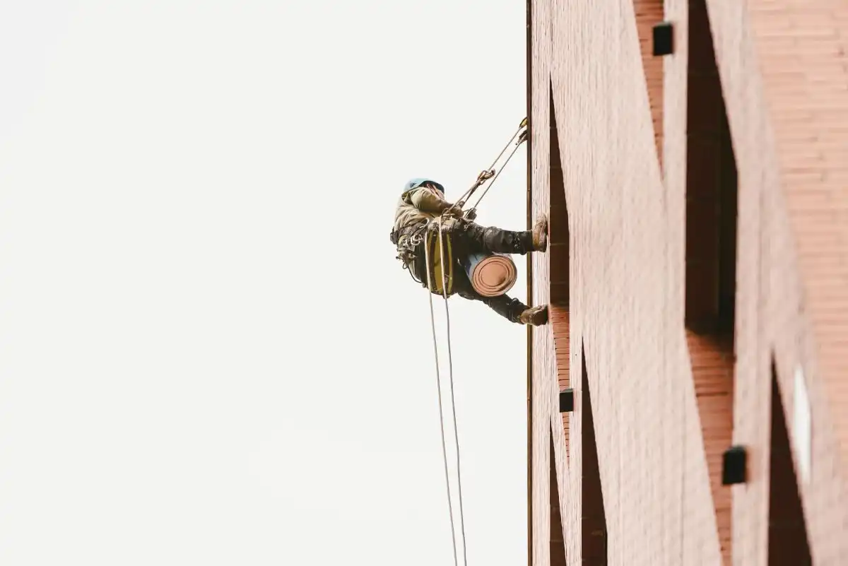 Alpinist utilitar care coboară pe corzi lângă o fațadă din cărămidă