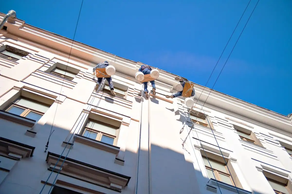 Trei alpiniști utilitari pe fațada unei clădiri cu ferestre