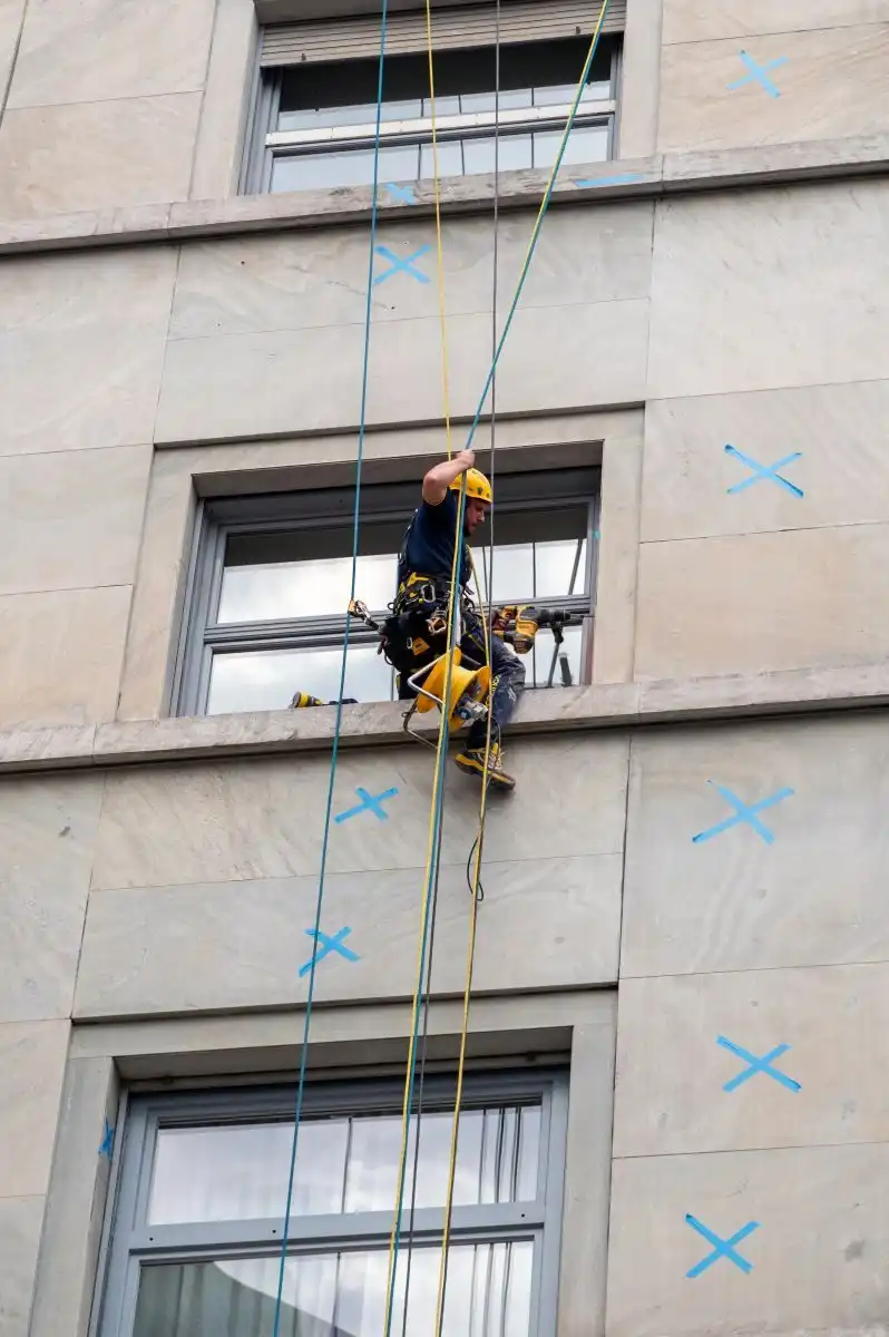 Alpinist utilitar pe corzi pe o fațadă cu marcaje albastre