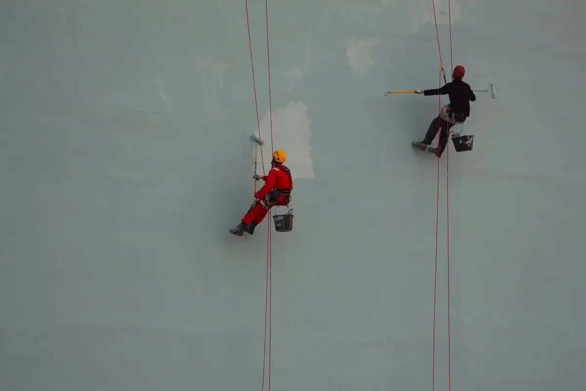 Doi alpiniști utilitari care vopsesc un perete înalt