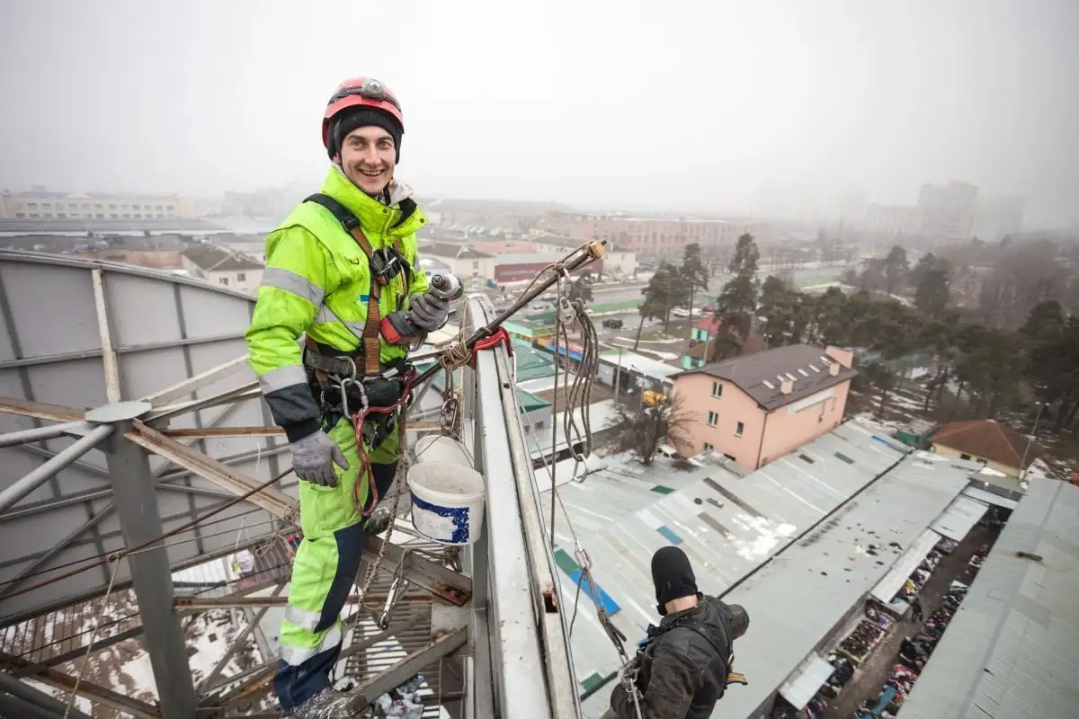 Alpinist utilitar pe acoperișul unei hale, deasupra unui depozit