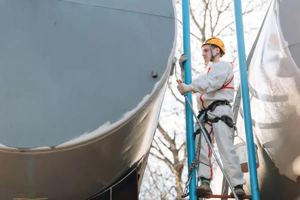 Alpinist utilitar în combinezon lângă un rezervor, sprijinit de o conductă