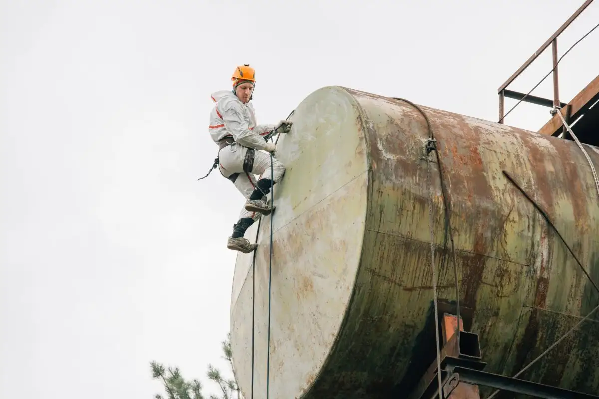 Alpinist utilitar care coboară pe un rezervor ruginit