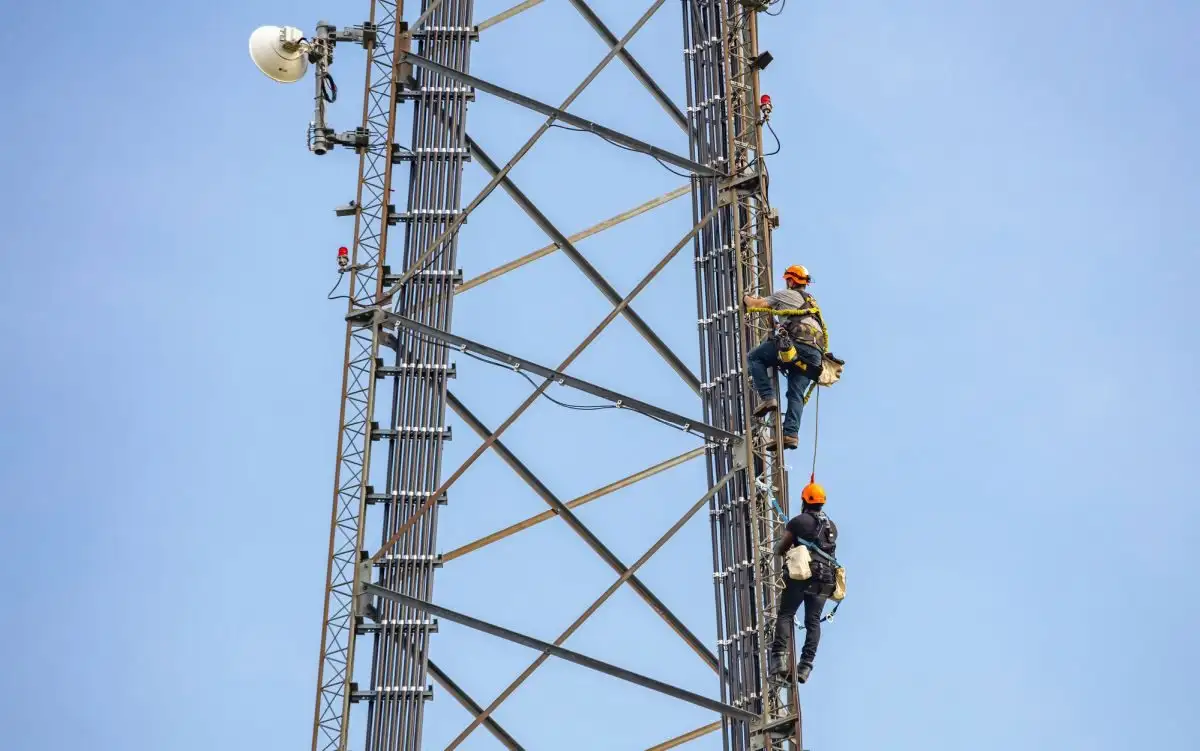 Doi alpiniști utilitari pe un pilon metalic de telecomunicații
