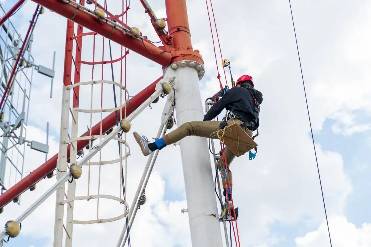 Alpinist utilitar pe corzi lângă un pilon metalic de telecomunicații