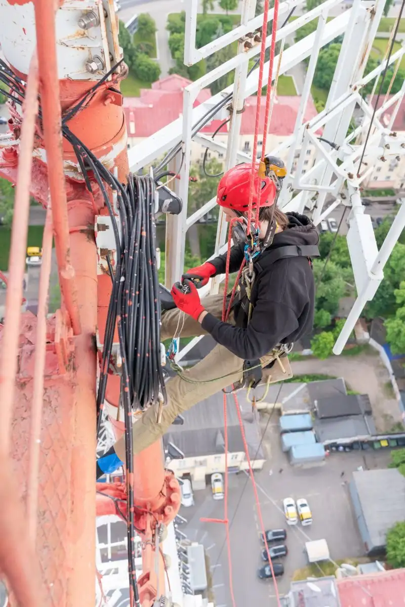 Alpinist utilitar care lucrează la cablurile de pe un turn metalic înalt